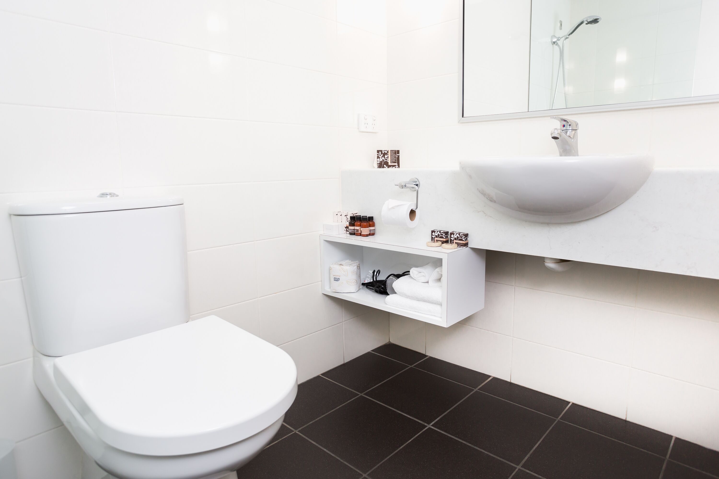 Ein modernes Badezimmer mit Toilette, Waschbecken mit Spiegel darüber und Ablage für Toilettenartikel.