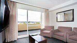 Habitación de hotel con un amplio ventanal corredero que da a un balcón, un televisor de pantalla plana montado en la pared, un conjunto de sofás y una mesa de centro.
