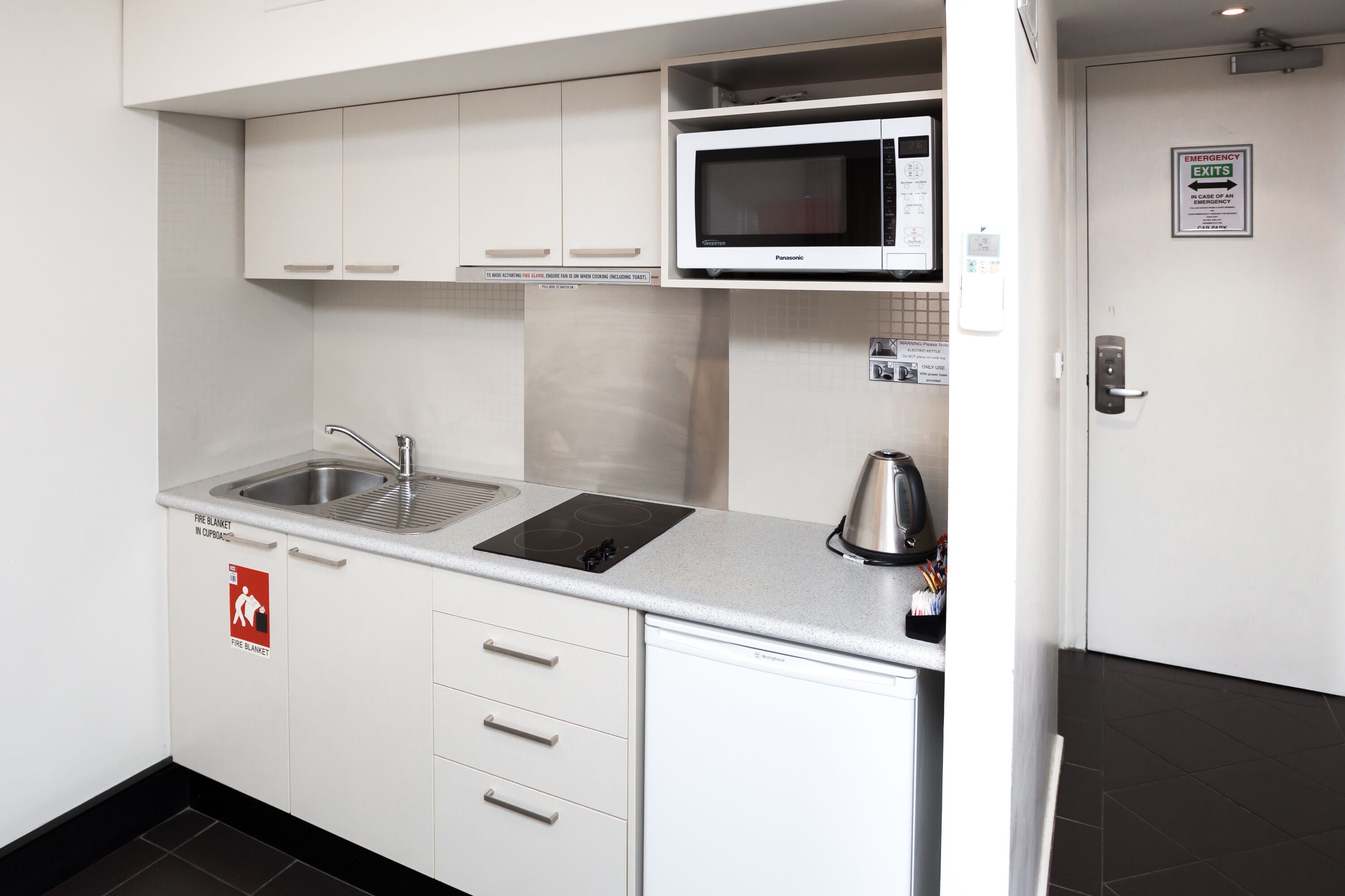 A modern kitchen with white cabinets, a stainless steel sink, a microwave, and a fire blanket sign.