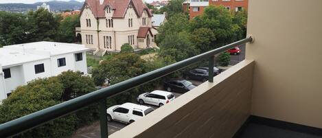 Vista desde un balcón sobre un estacionamiento con varios coches, un edificio de techo rojo y una torre distante.