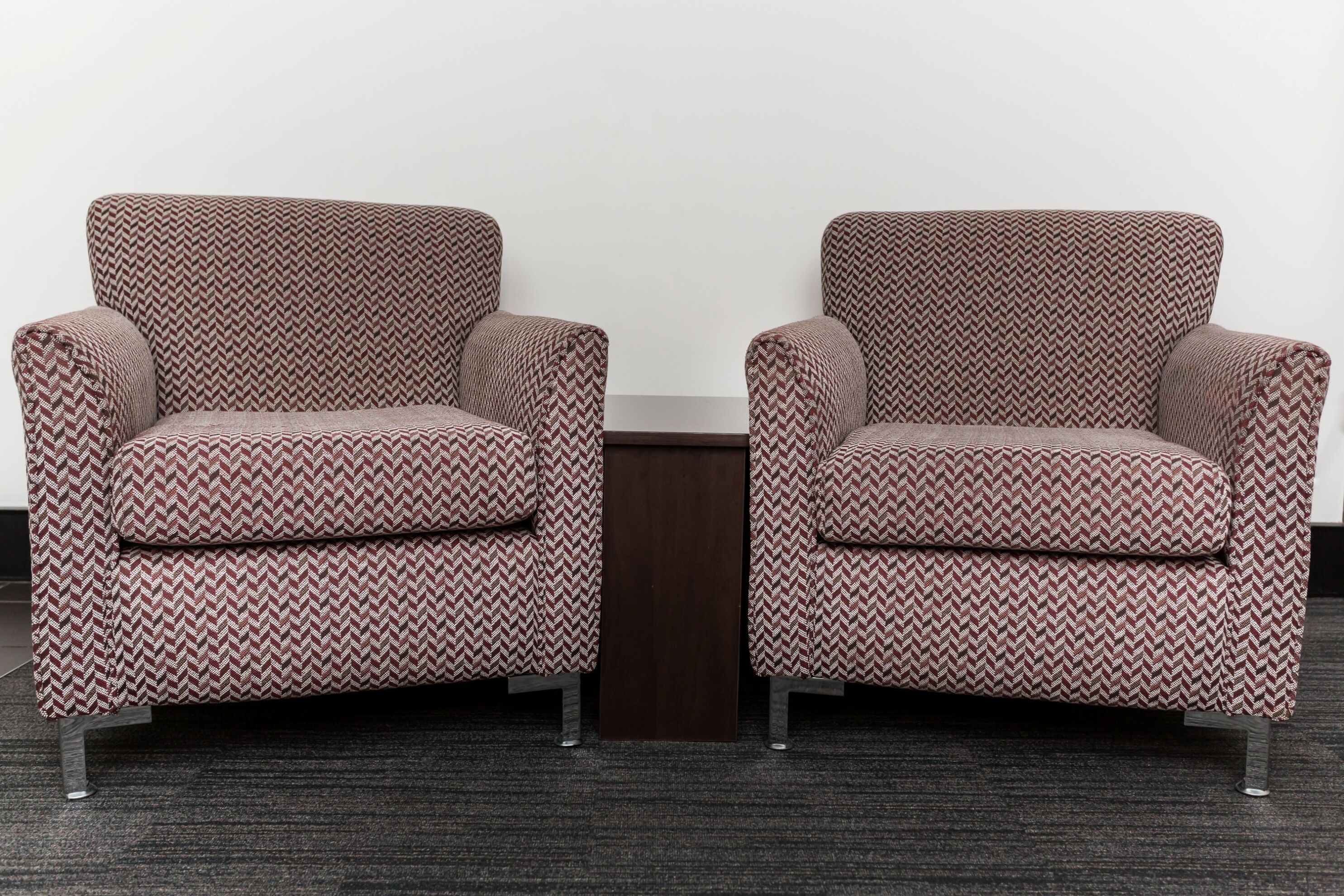 Deux fauteuils à motif chevrons, une petite table d’appoint en bois et un sol recouvert d’une moquette sombre.
