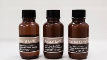 Three brown bottles labeled 'Natural Earth+ Pure New Zealand Active Manuka Honey' with different product names: SHAMPOO, CONDITIONER, and MOISTURISER.