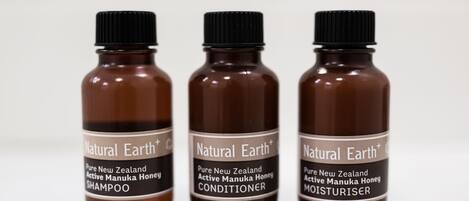 Three brown bottles labeled 'Natural Earth+ Pure New Zealand Active Manuka Honey' with different product names: SHAMPOO, CONDITIONER, and MOISTURISER.