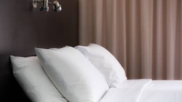 A neatly made bed with white bedding and pillows, a dark headboard, and a wall-mounted light fixture.