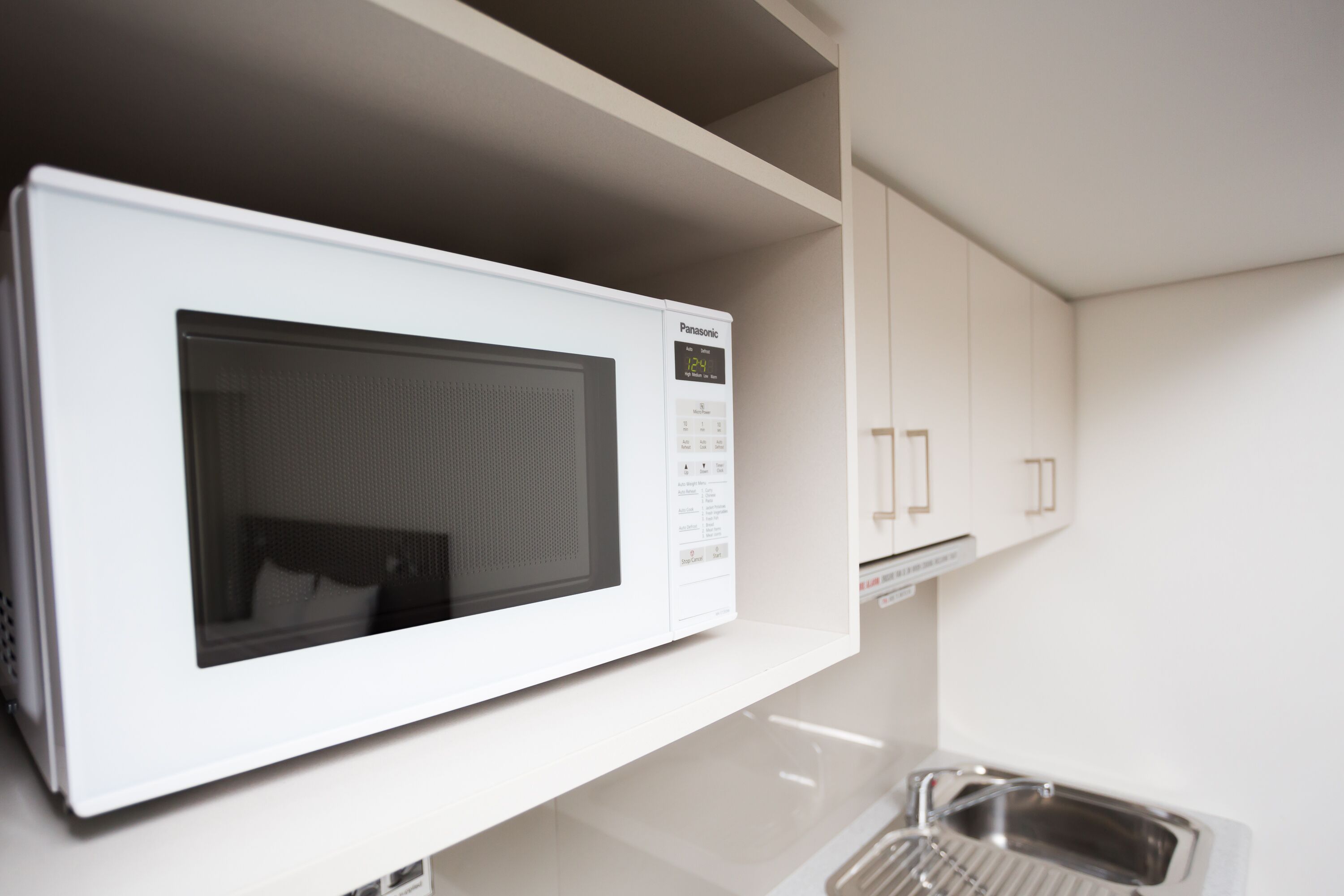 Un forno a microonde bianco su un piano di lavoro bianco in una cucina con mobili bianchi.