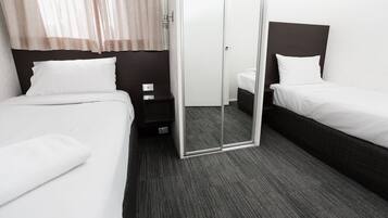 Quarto de hotel com duas camas, uma porta de correr de vidro e chão coberto por carpete escuro.