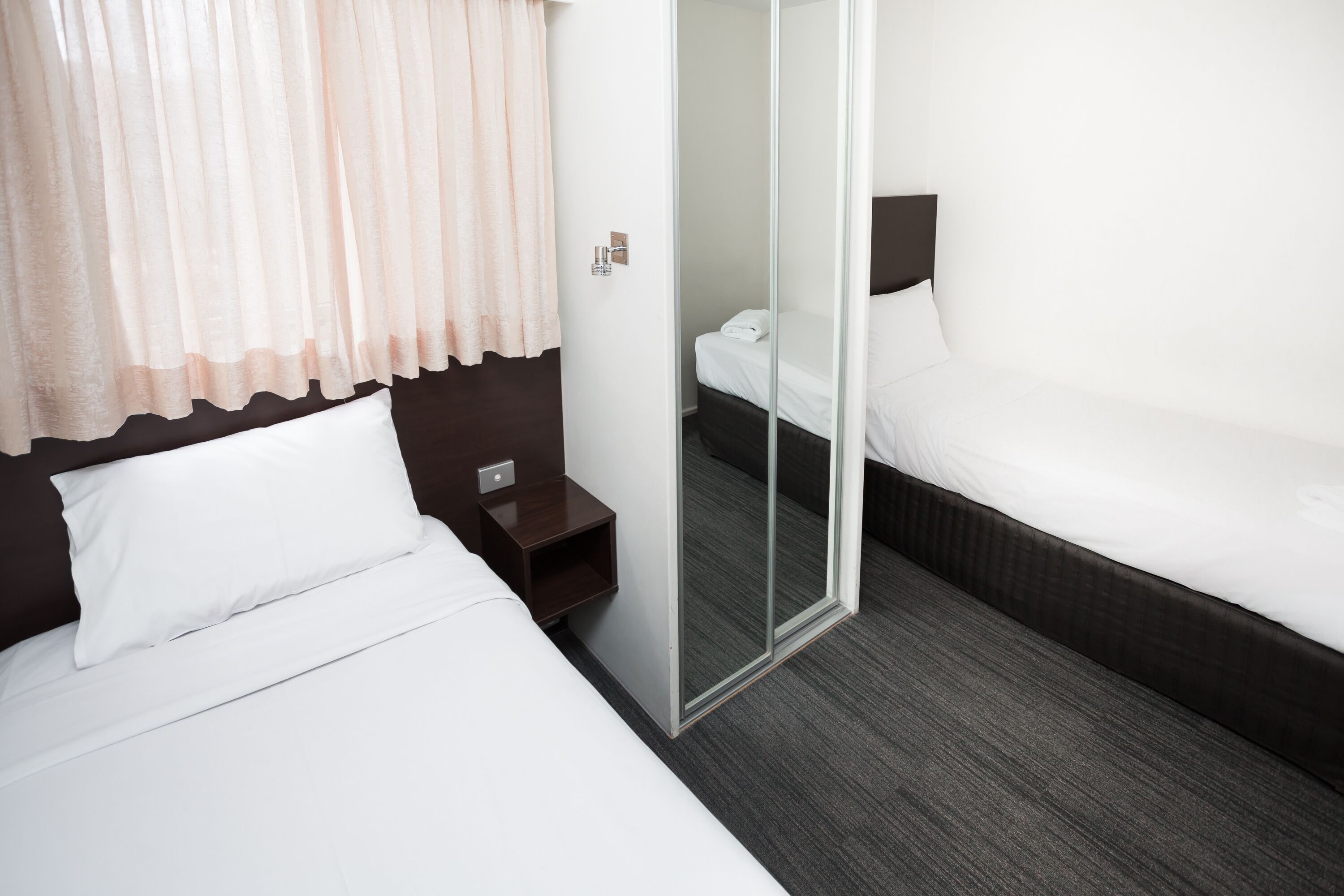 A hotel room with two beds, a nightstand, a mirror, and a door leading to a bathroom.