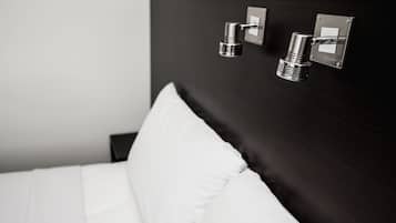 A modern hotel room with a neatly made bed, a dark headboard, and wall-mounted lighting fixtures.