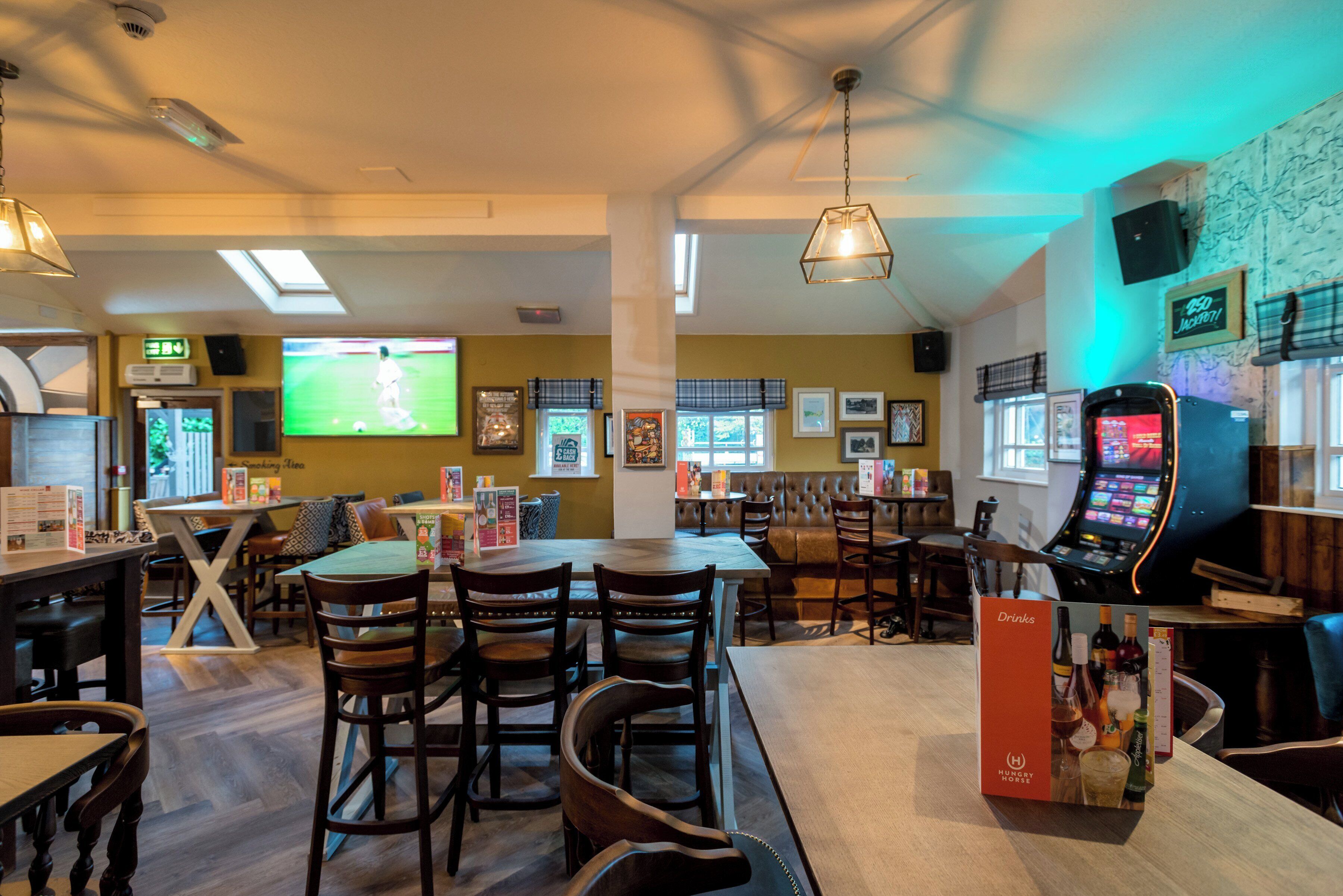 A restaurant with multiple tables and chairs, a television screen, and a jukebox.