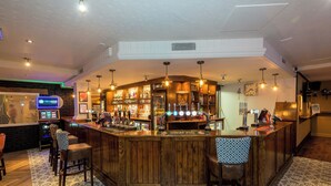Una zona de bar con mostradores de madera, taburetes y una variedad de botellas y copas.