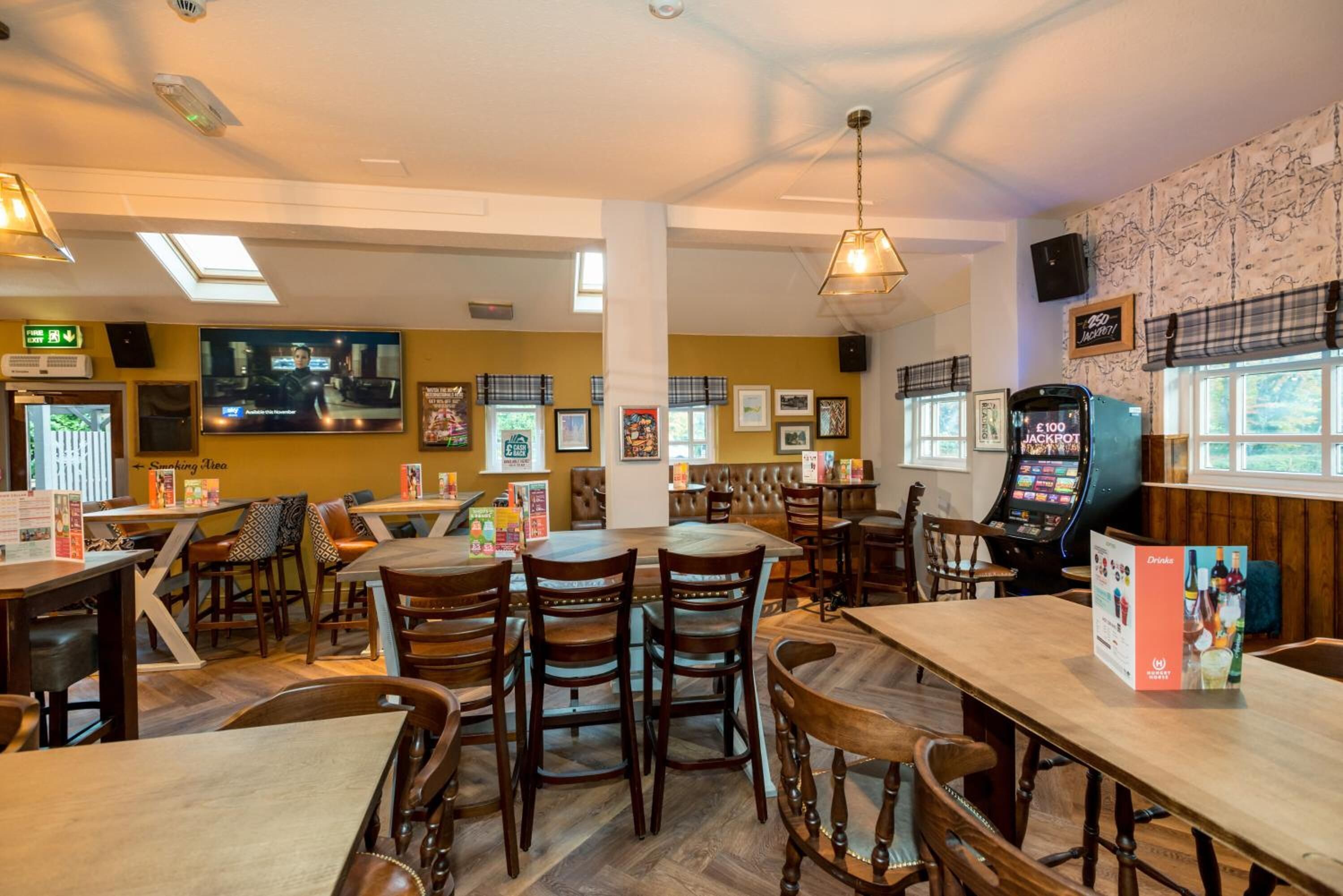 Un restaurante con mesas y sillas de madera, un jukebox y una pantalla de televisión.
