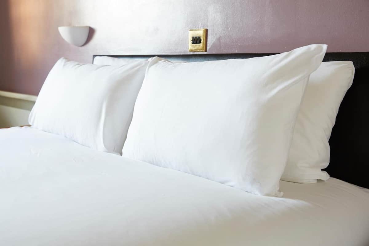 A neatly made bed with white linens and a headboard with a light switch.