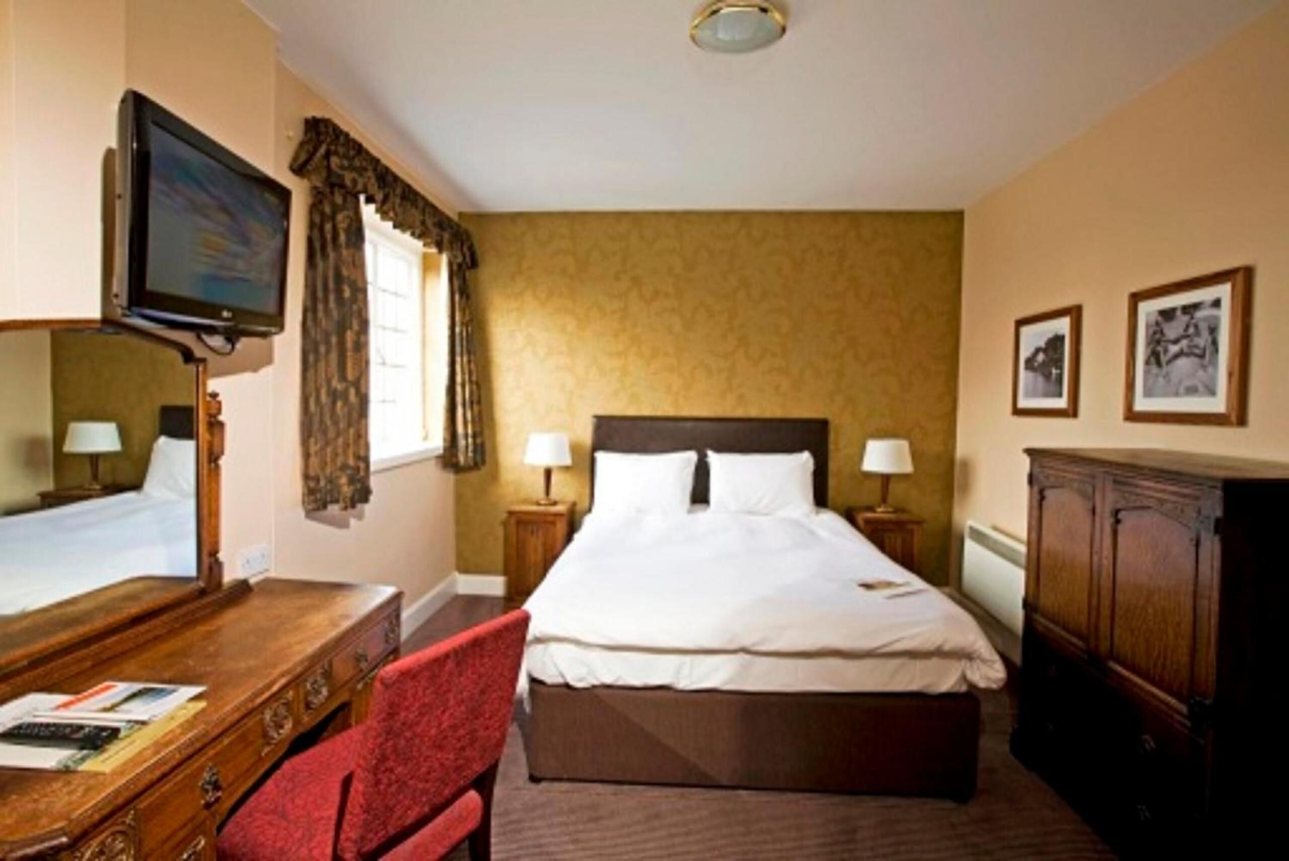 A hotel room with a large bed, a desk with a chair, a television, and two bedside lamps.