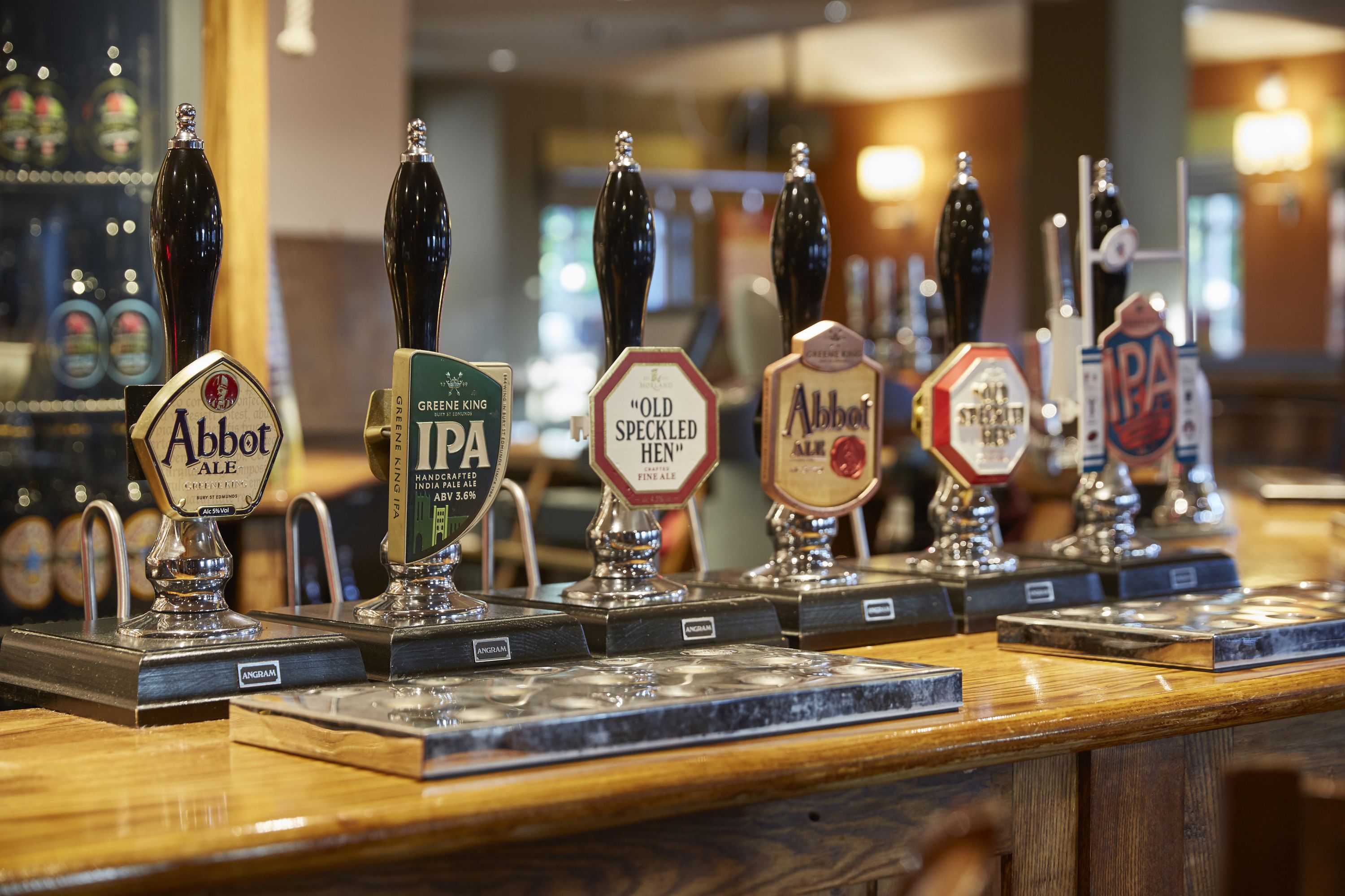 A bar counter with various beer taps labeled with names like Abbot, IPA, and Old Speckled Hen.