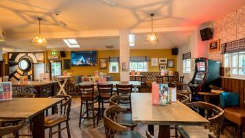 A restaurant with wooden tables and chairs, a jukebox, and a large screen displaying a movie.