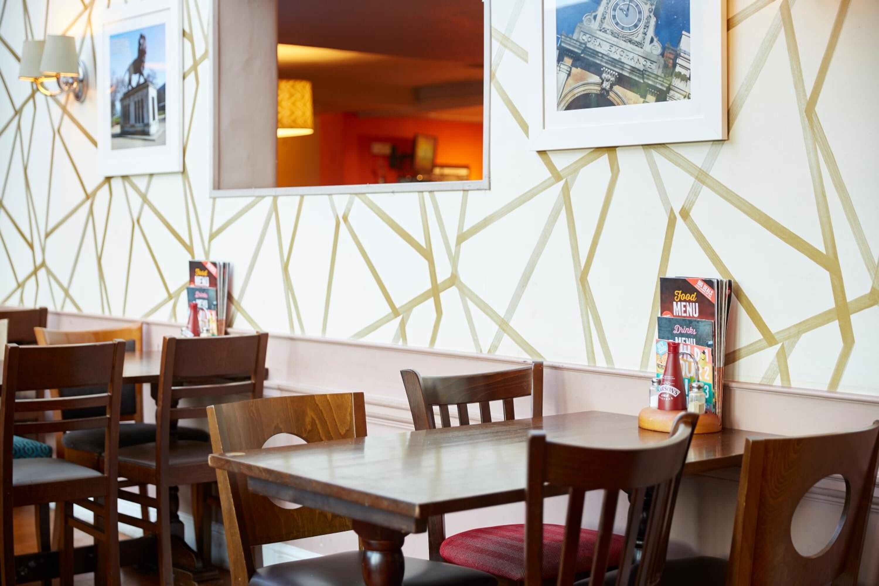 Un interior de restaurante con mesas y sillas de madera, cuadros en la pared y un atril para el menú.