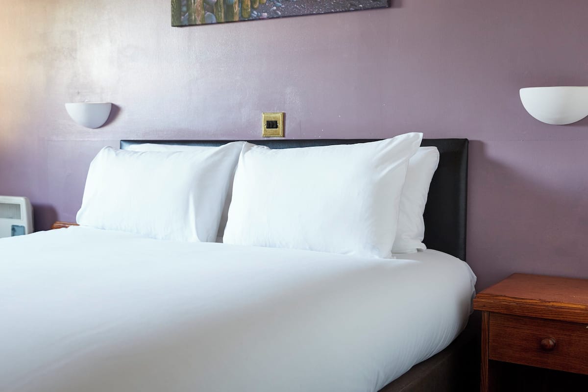 A neatly made bed with white linens in a room with purple walls.