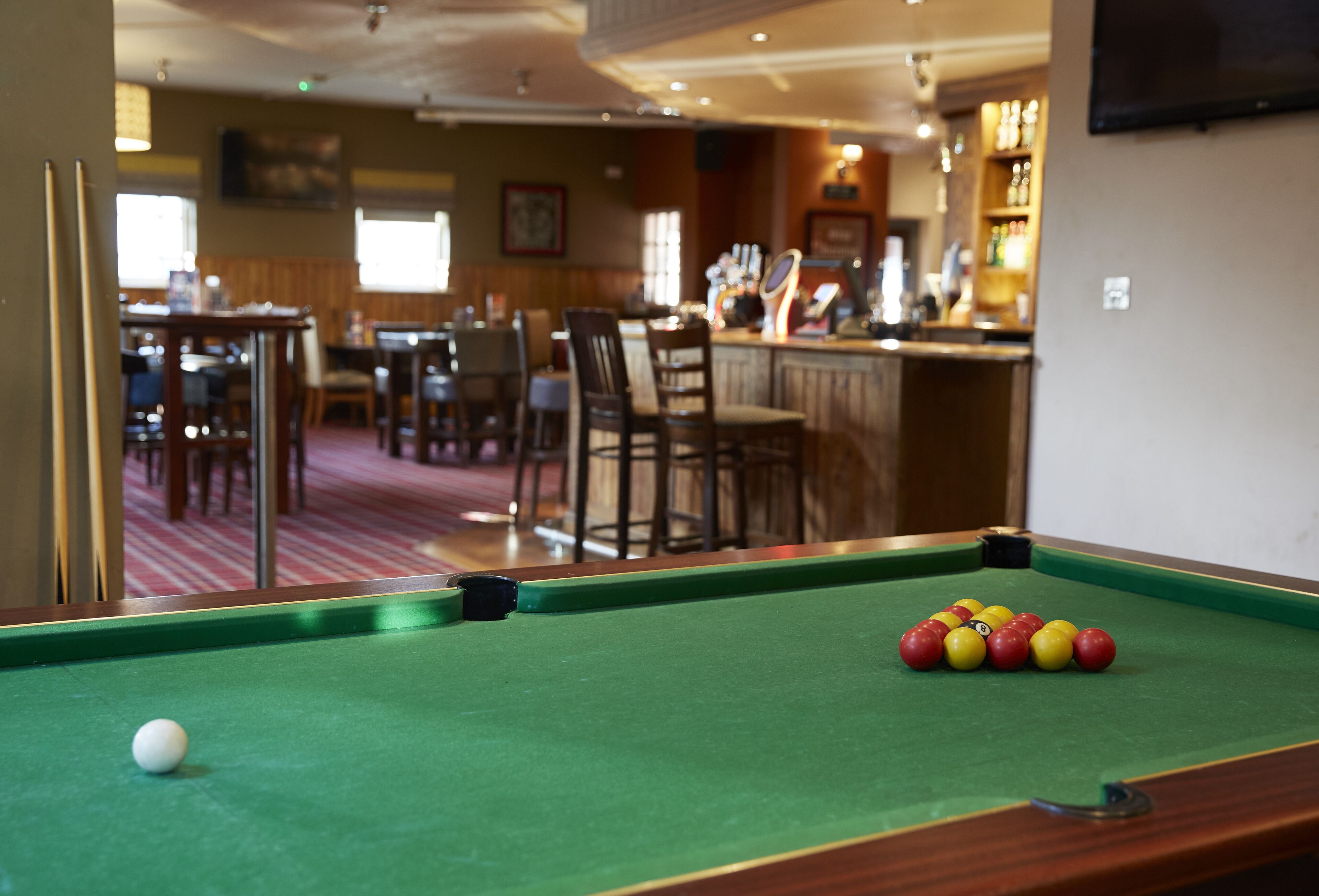 Una mesa de billar con bolas y una bola blanca, una zona de bar con televisor, y un comedor con sillas y mesas.
