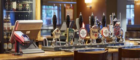 A bar area with wooden bar counters, a cash register, and beer taps labeled with various beer types.