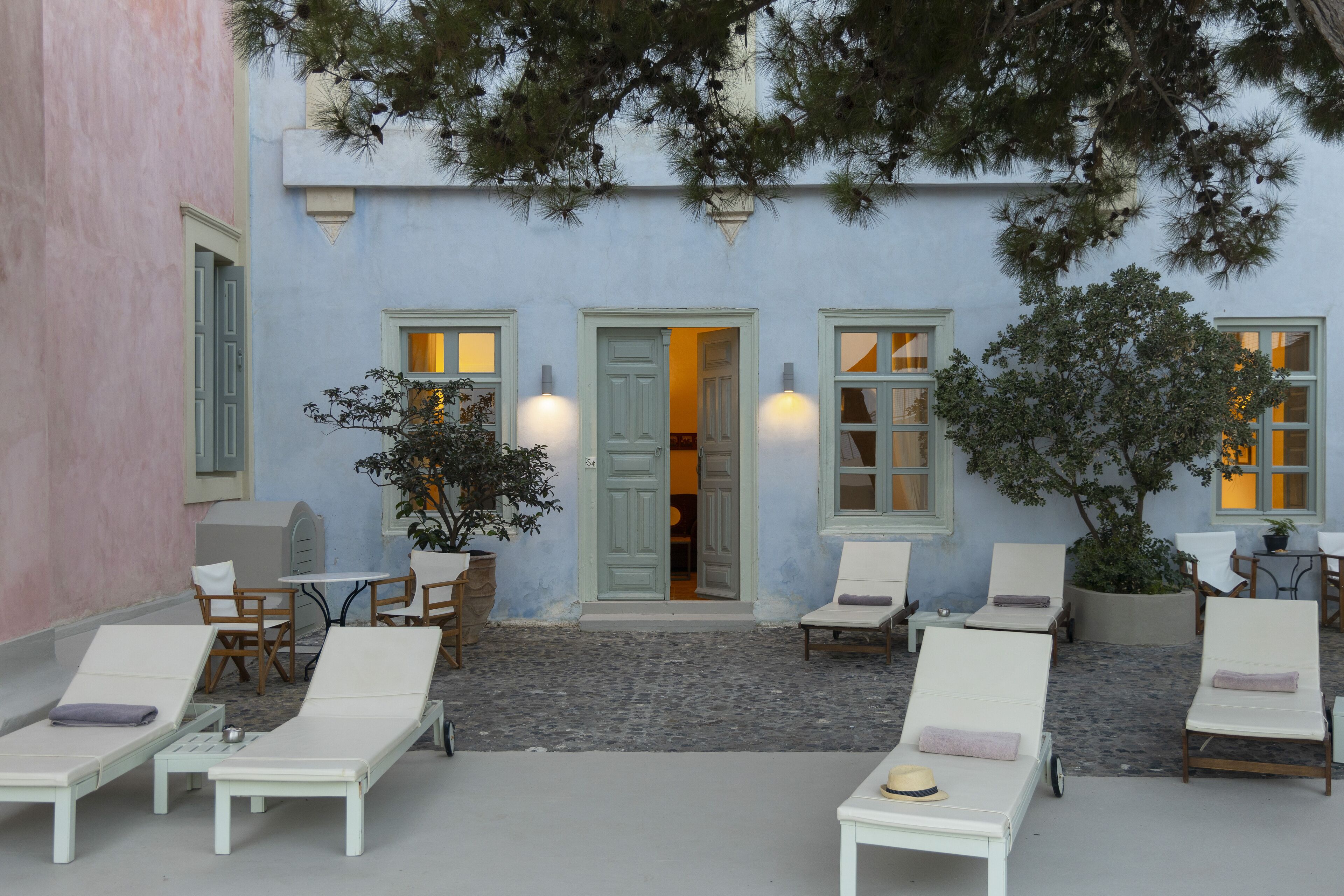 A courtyard with lounge chairs, a table, and a potted plant.