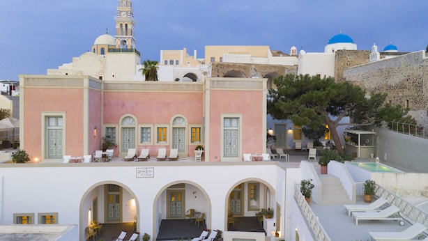 Un hotel con fachada rosa, varios balcones con sillones de descanso y una zona de piscina.
