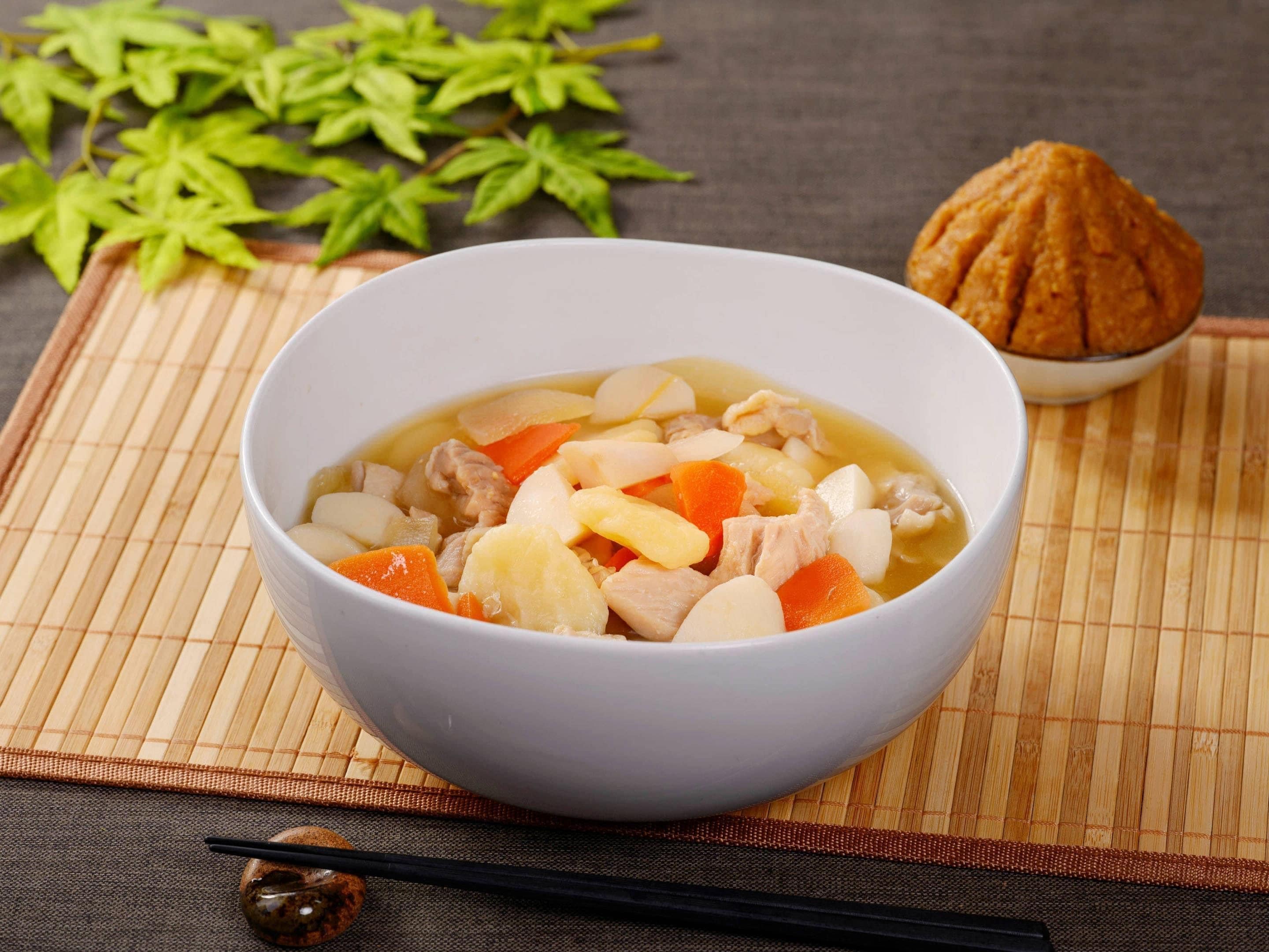 Un bol de soupe contenant des légumes et de la viande, posé sur un tapis en bambou.