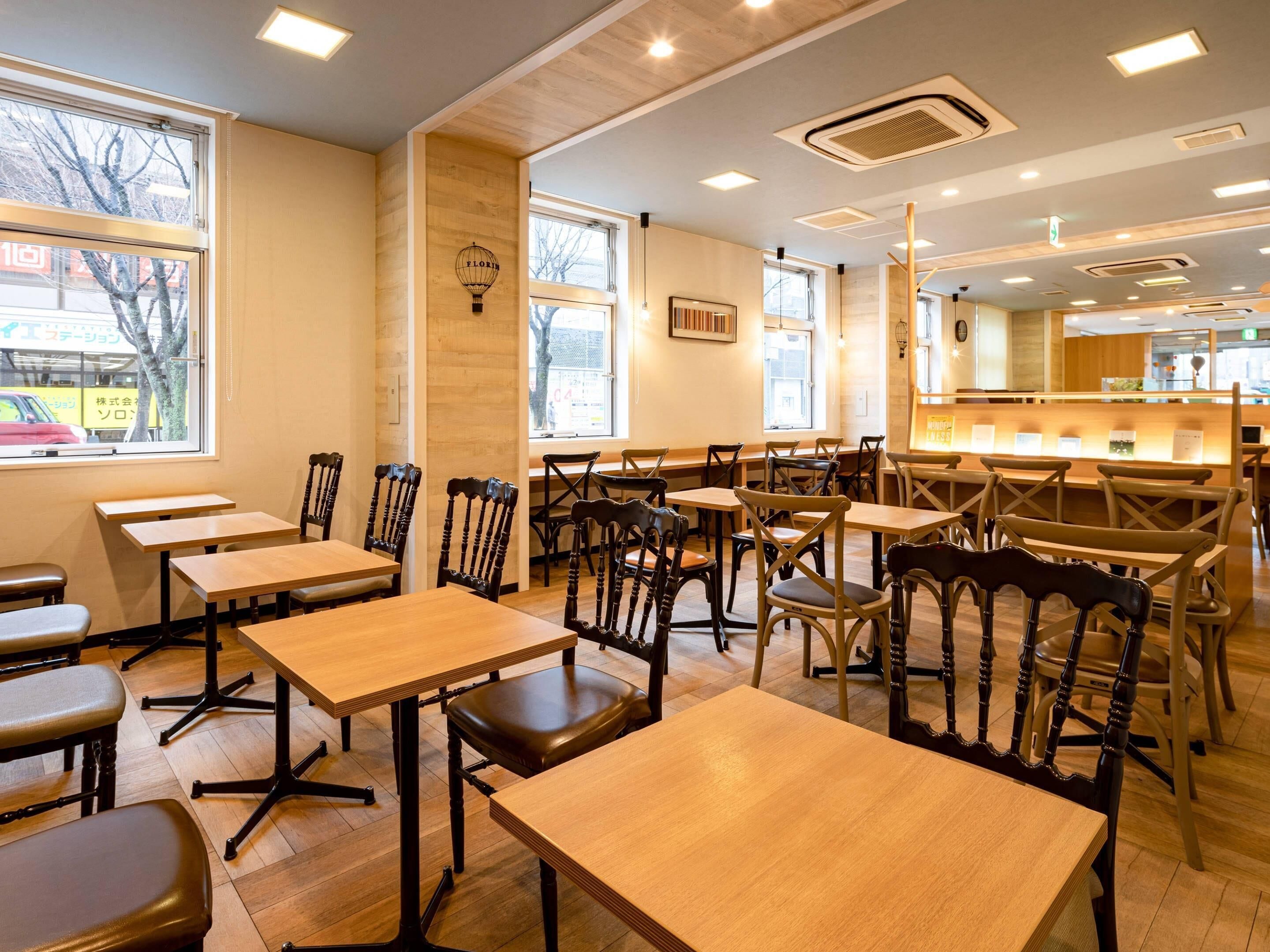 A restaurant with wooden tables and chairs, large windows, and a counter area.