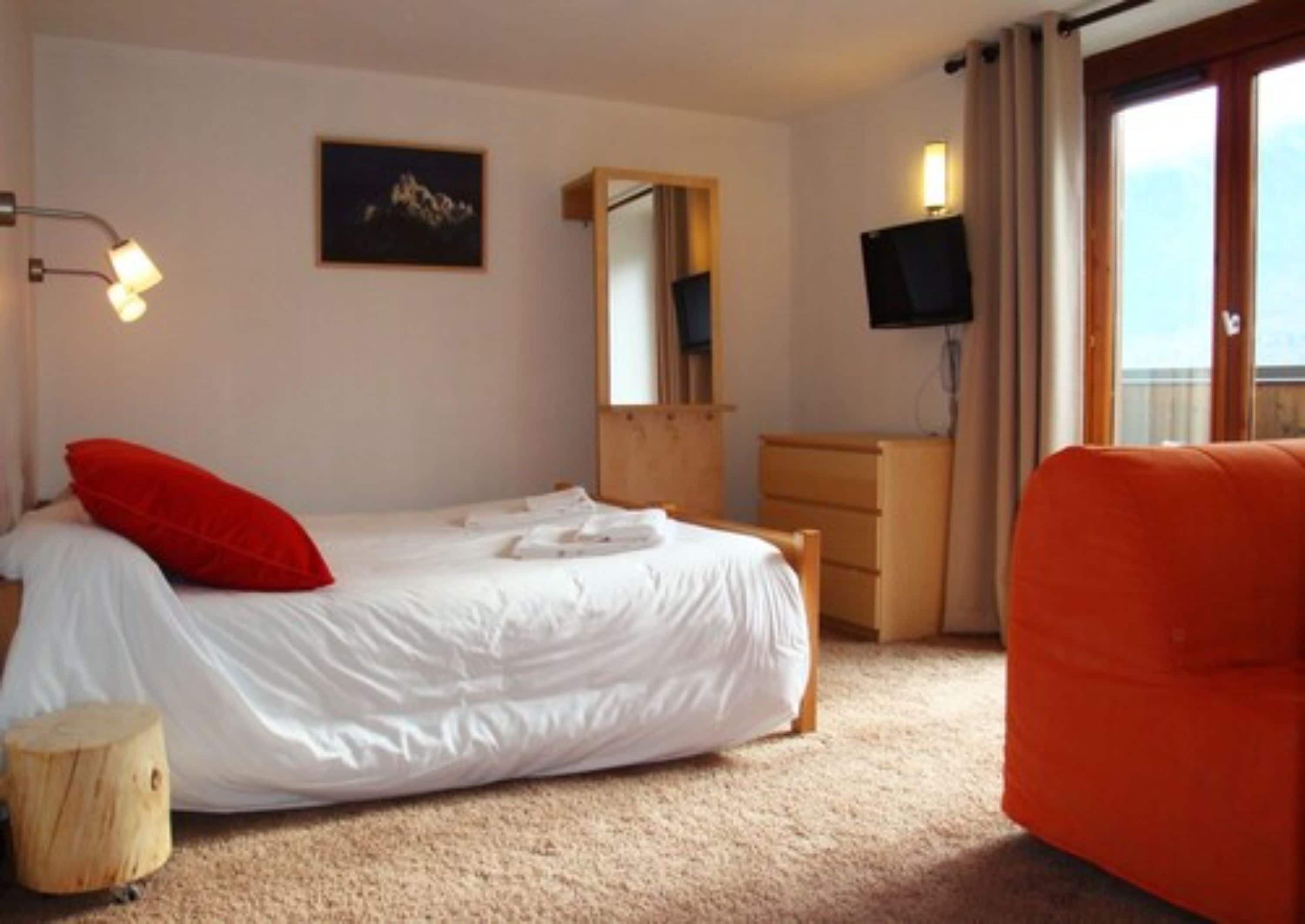 Ein Schlafzimmer mit Bett, Kommode, Fernseher und Fenster.