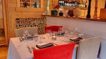 A dining area with a table set for four, a wooden wall with a log display, and a shelf with wine bottles.