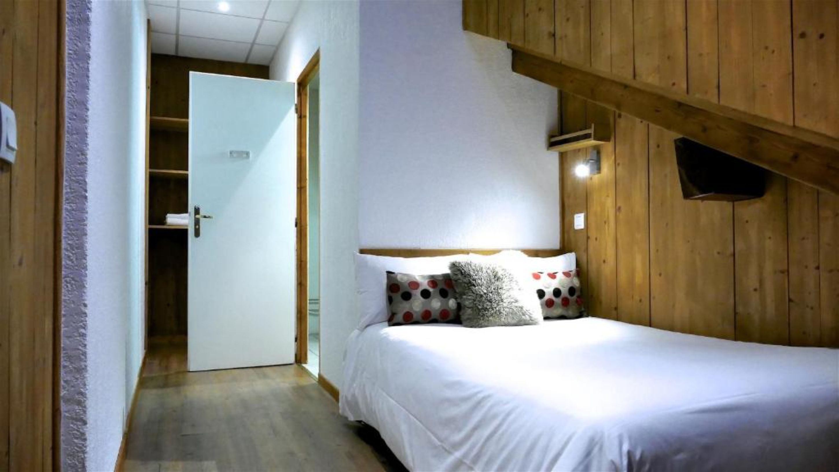 A bedroom with a wooden ceiling, a bed with white bedding, and a polka-dotted pillow.