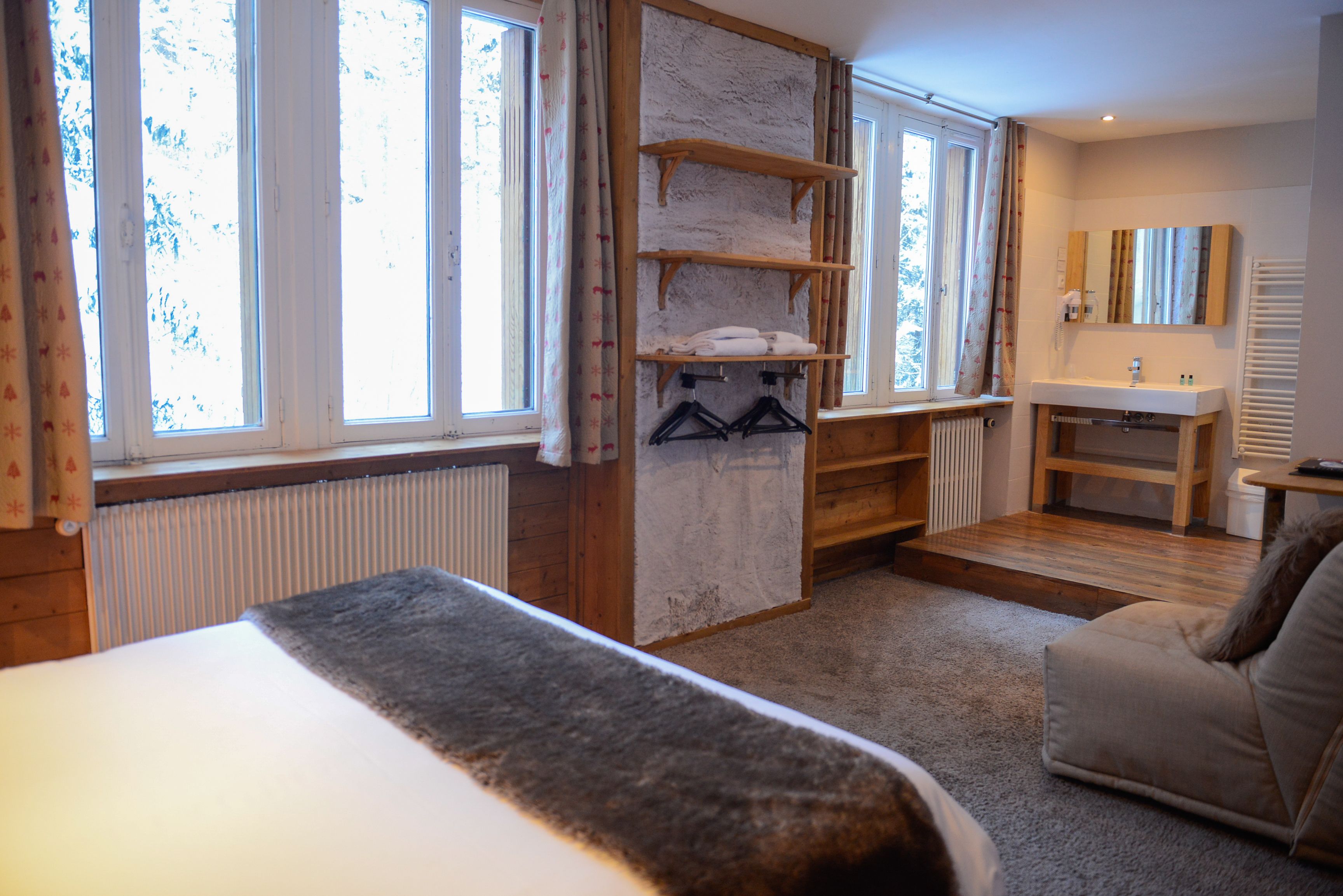 Ein Schlafzimmer mit Bett, einer Holzhängeregalschrank, einem Badezimmer mit Waschbecken und Spiegel sowie großen Fenstern.