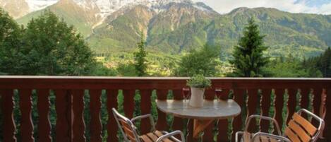 A balcony with two chairs and a table, overlooking a mountainous landscape with snow-capped peaks.