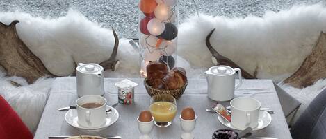 A breakfast setup with a table, cups, eggs, toast, and a fruit bowl.