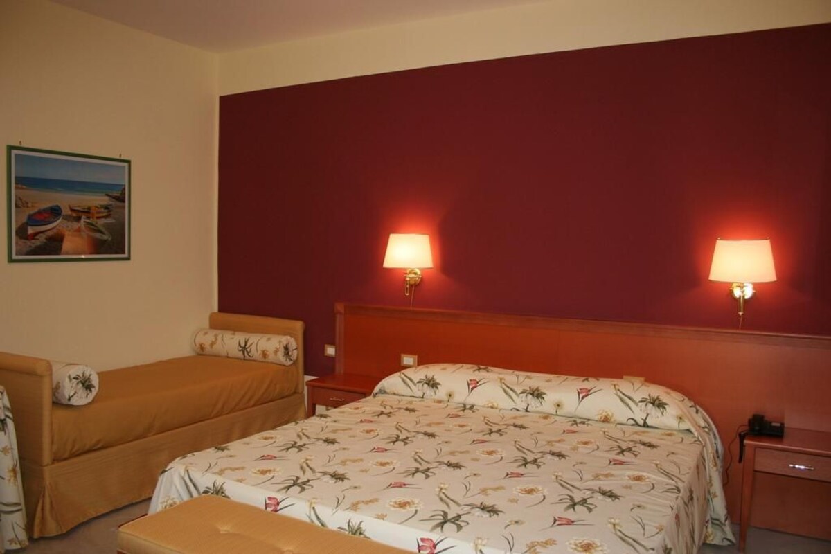 A hotel room with a large bed, two bedside tables, a nightstand, a bench, and a painting on the wall.