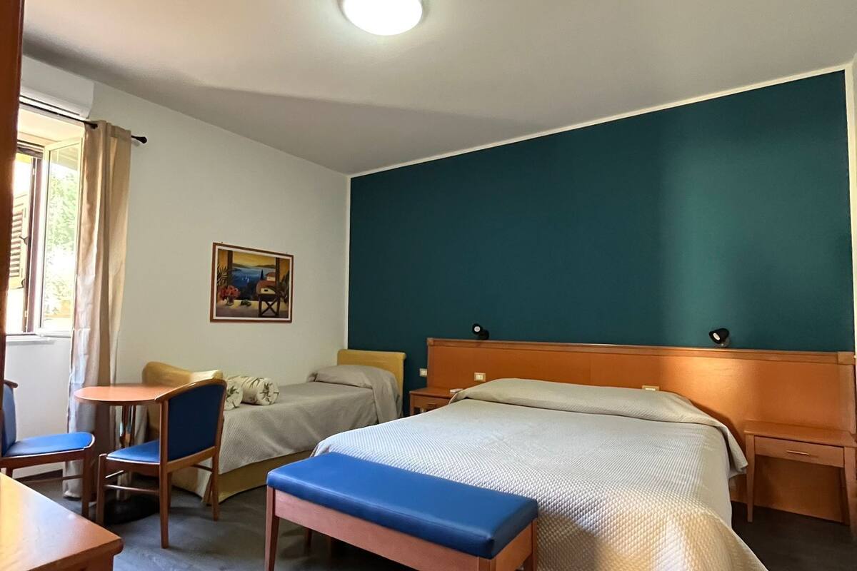 A hotel room with a bed, a desk, a chair, a bench, and a painting on the wall.