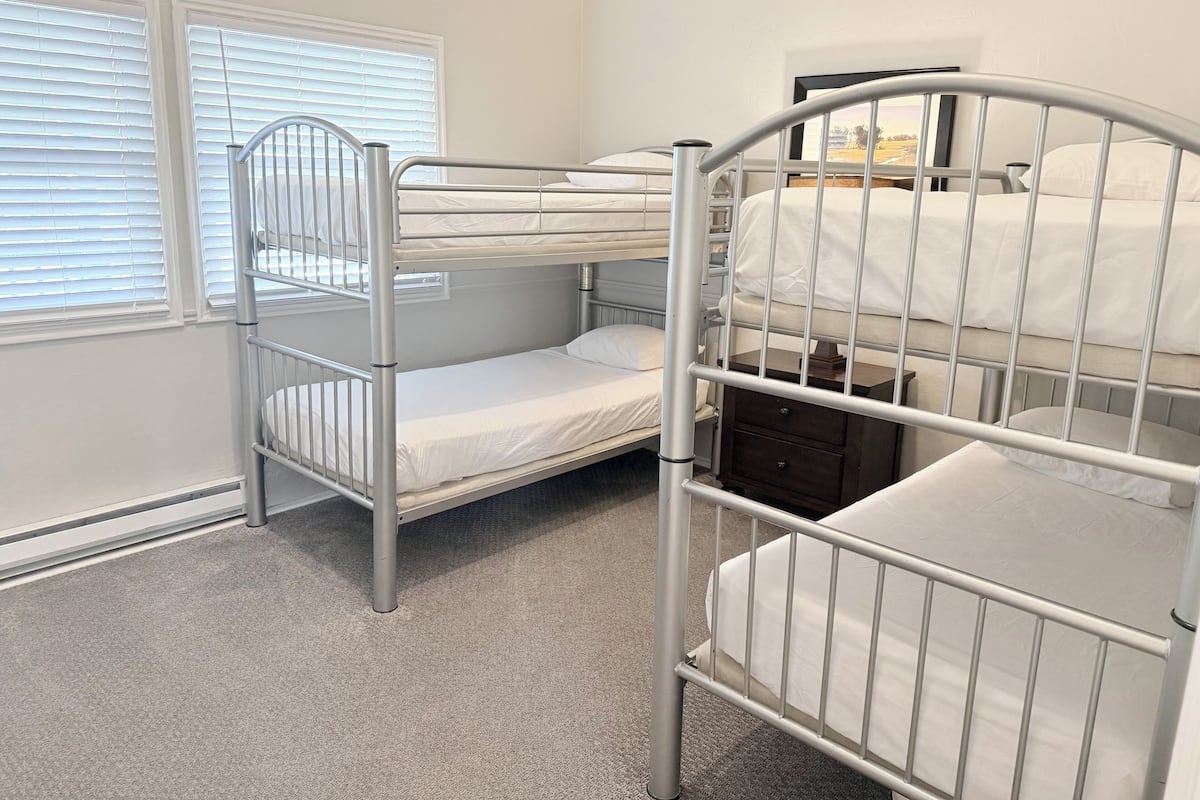 A bunk bed room with a window, a bedside table, and a radiator.