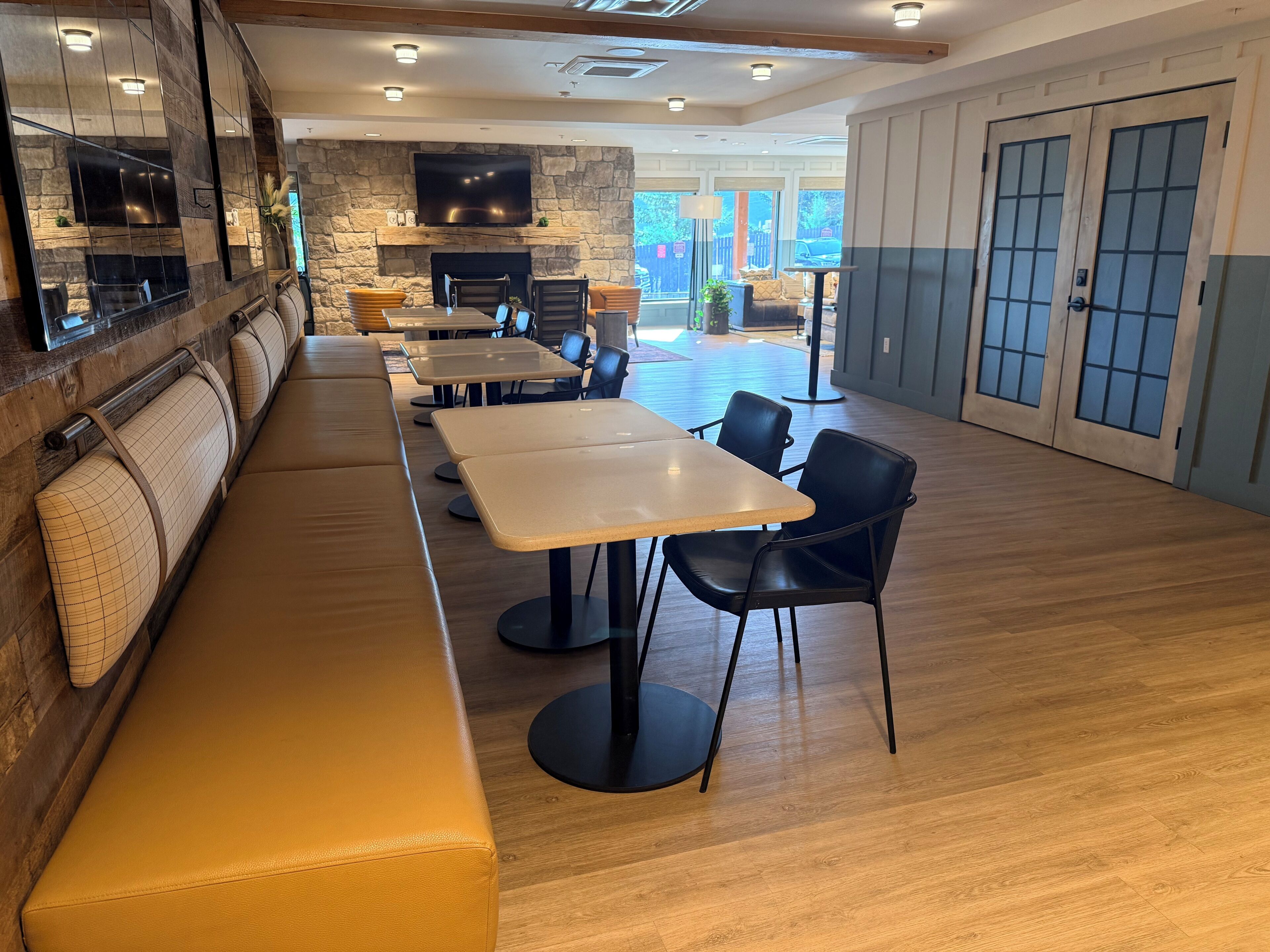 A restaurant with a stone wall, a flat-screen TV, wooden tables, black chairs, and a wooden bench.