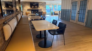 A restaurant with a stone wall, a flat-screen TV, wooden tables, black chairs, and a wooden bench.