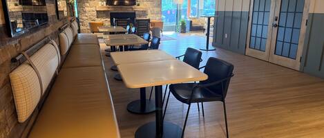 A restaurant with a stone wall, a flat-screen TV, wooden tables, black chairs, and a wooden bench.