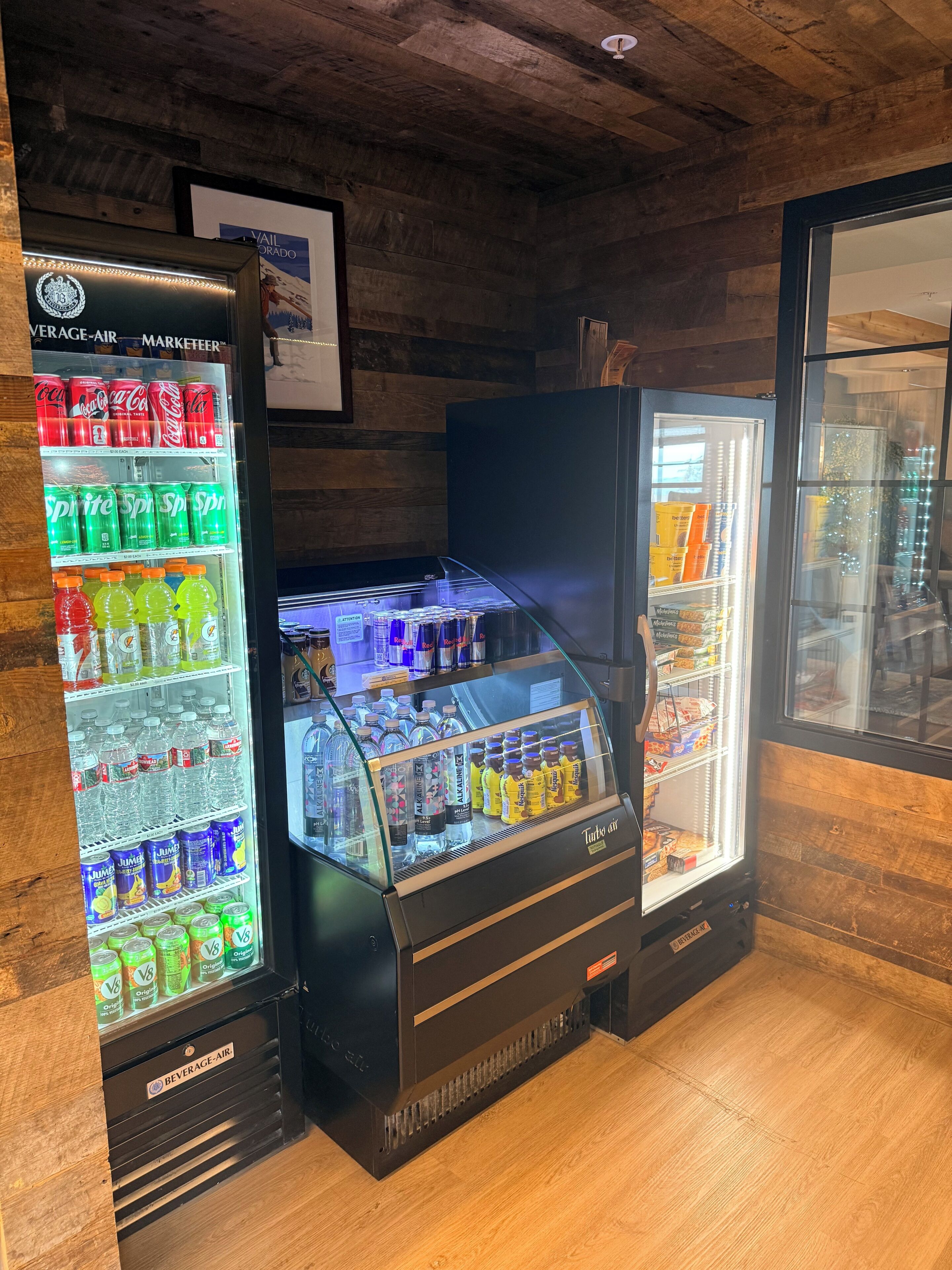 Un enfriador de bebidas con varias opciones, un refrigerador pequeño con aperitivos y una pared de madera.