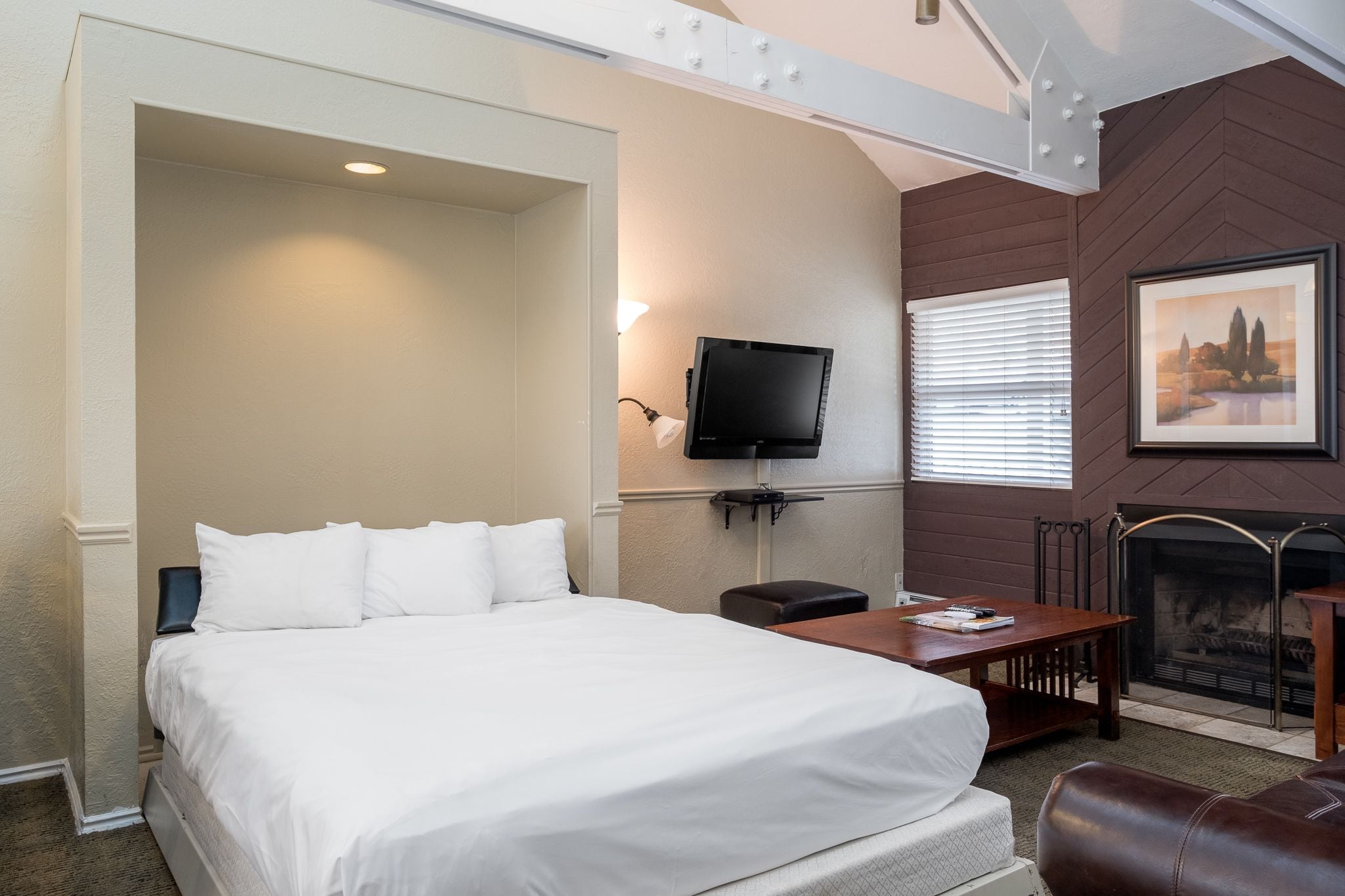 A hotel room with a large bed, a TV mounted on the wall, a fireplace, and a dining table.