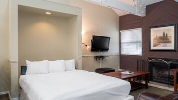 A hotel room with a large bed, a TV mounted on the wall, a fireplace, and a dining table.