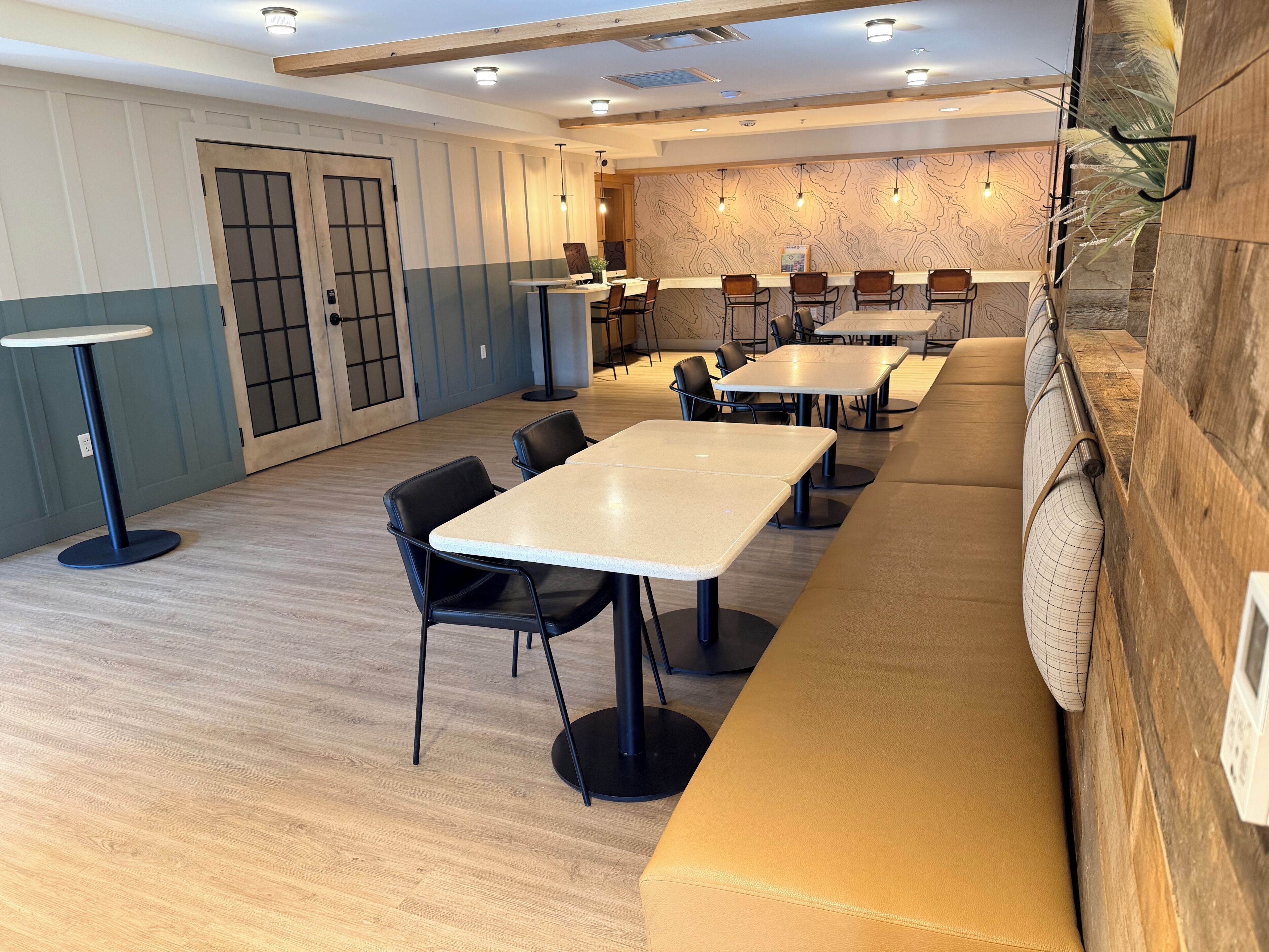 Un comedor moderno con varias mesas y sillas, un banco largo y una pared de acento de madera.