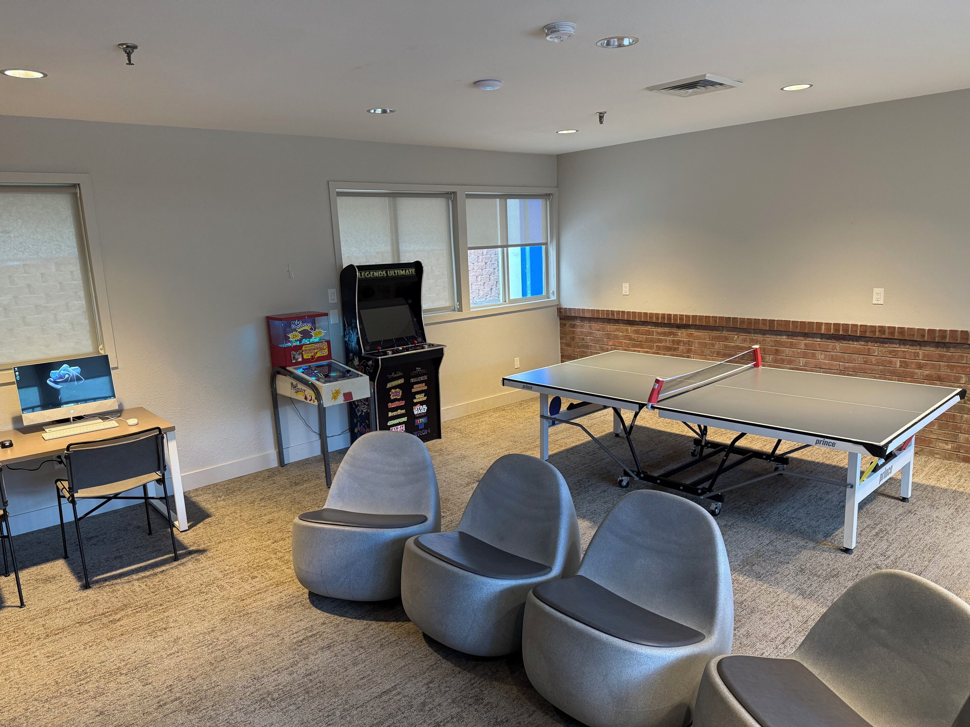 A room with a ping pong table, gaming console, and comfortable seating.