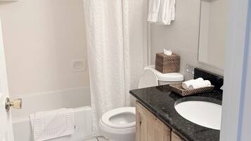 A bathroom with a shower, toilet, sink, and mirror.