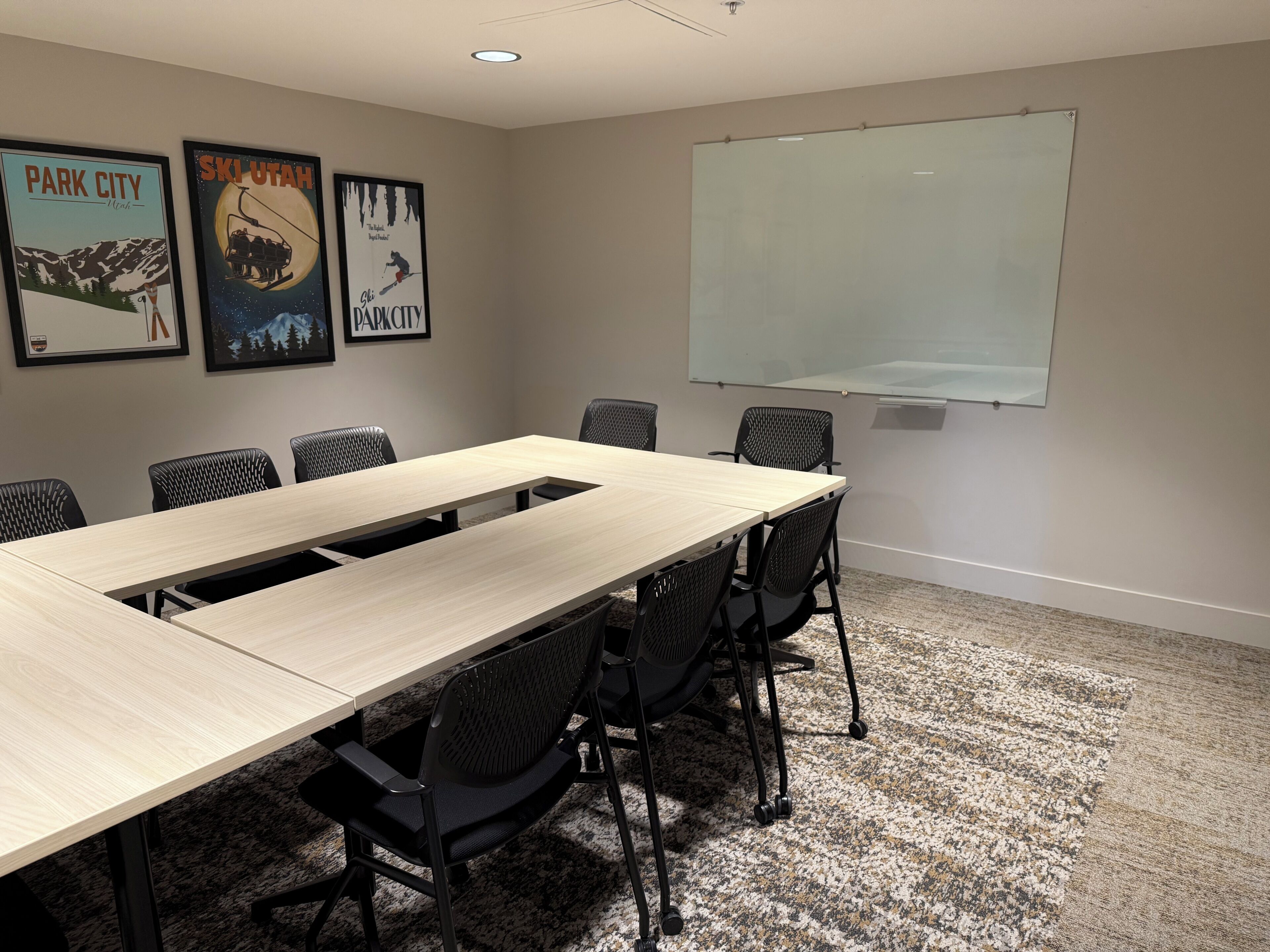Una sala de conferencias con una mesa larga, seis sillas, una pantalla de proyector y tres carteles en la pared.