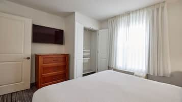 Hotelkamer met een groot bed, een houten dressoir, een televisie, een inloopkast en een raam met gordijnen.