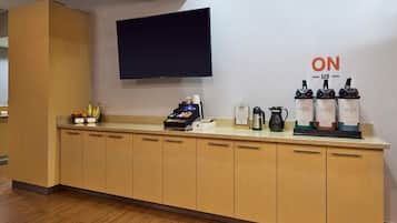 Zona de recepción de hotel con un televisor de pantalla plana en la pared, una máquina de café y una exhibición de botellas de agua caliente.
