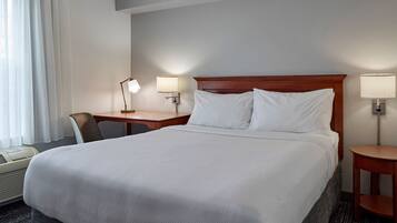 Una habitación de hotel con una cama grande, dos mesitas de noche, un escritorio, una silla y dos lámparas de pared.