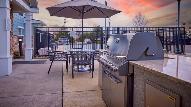Eine Terrasse im Freien mit Grill, Tischen und Sonnenschirm.